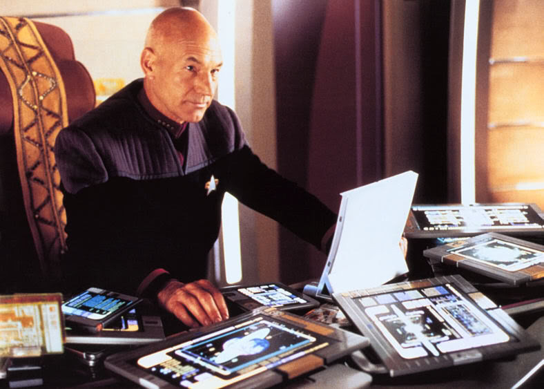 Captain Picard at his desk surrounded by tablets.